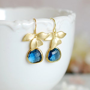 Puede incluir: Pendientes de oro con gotas de piedras preciosas azules y detalles de flores doradas.
