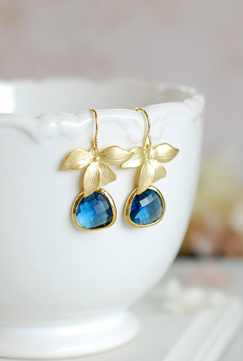 Puede incluir: Pendientes de oro con gotas de piedras preciosas azules y detalles de flores doradas.