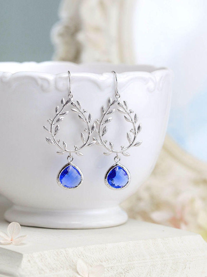 May include: Silver dangle earrings with a leaf design and a teardrop shaped blue gemstone.