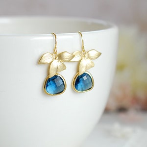 Puede incluir: Pendientes de oro con gotas de piedras preciosas azules y detalles de flores doradas.