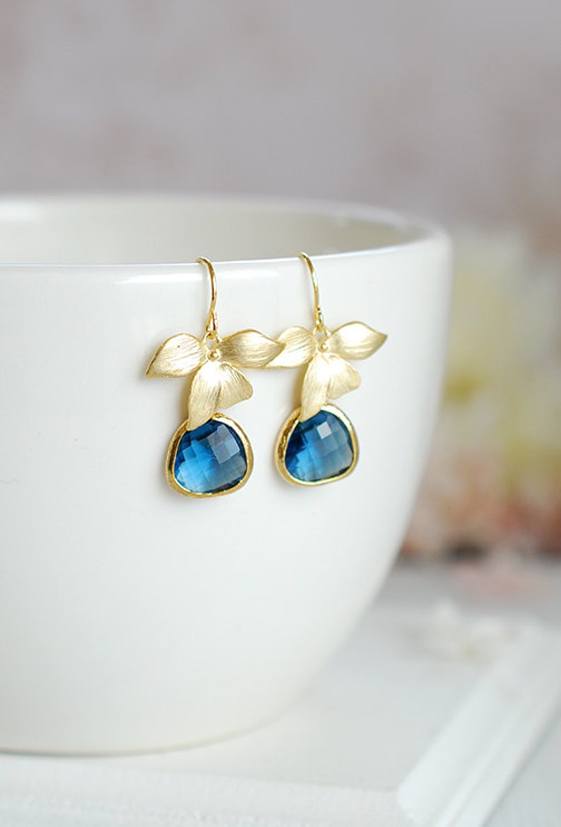 Puede incluir: Pendientes de oro con gotas de piedras preciosas azules y detalles de flores doradas.