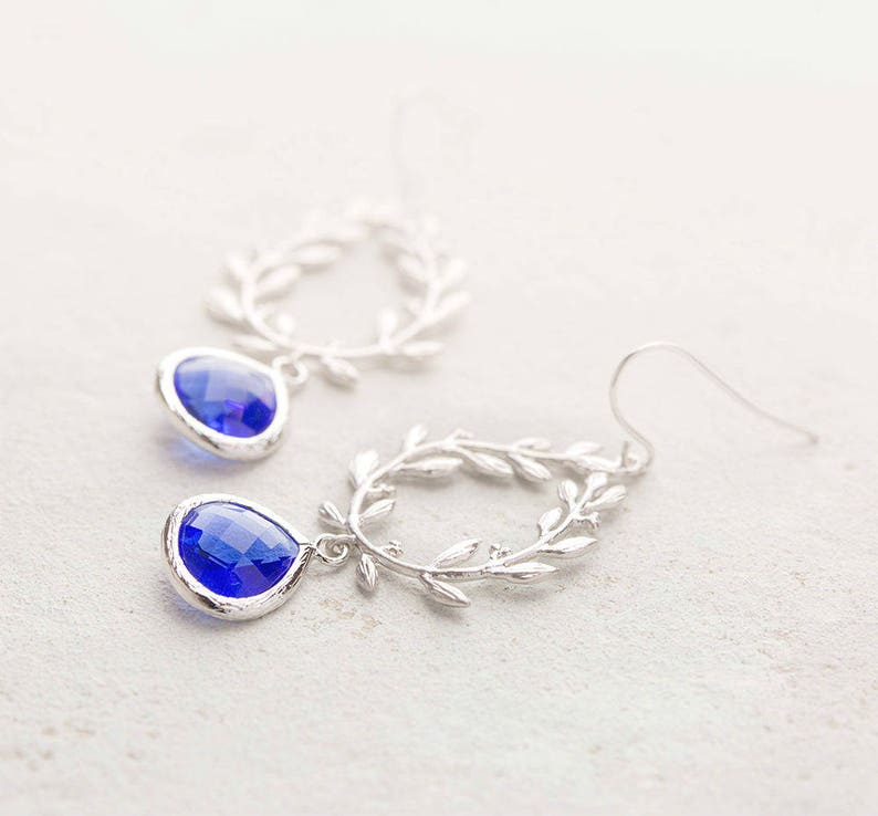 May include: Silver earrings with a blue teardrop-shaped crystal dangling from a silver leaf design.