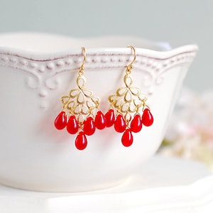 Peut inclure: Boucles d'oreilles pendantes dorées avec un motif floral délicat et des perles rouges en forme de larme.