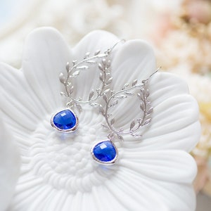 May include: Silver earrings with a delicate leaf design and a dangling blue gemstone.