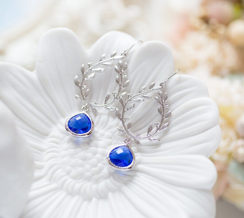 May include: Silver earrings with a delicate leaf design and a dangling blue gemstone.