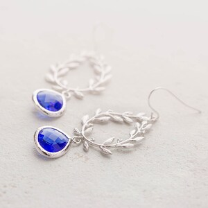 May include: Silver dangle earrings with a blue teardrop-shaped crystal and a delicate leaf design.