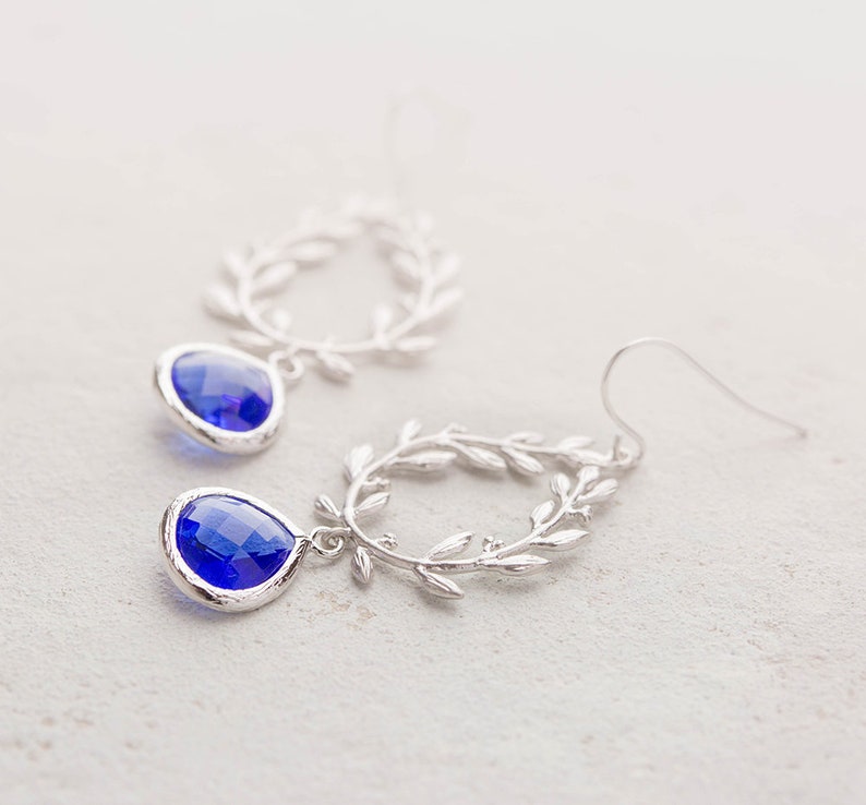 May include: Silver dangle earrings with a blue teardrop-shaped crystal and a delicate leaf design.