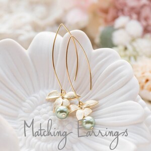 May include: Gold-coloured earrings featuring a floral design and a light green pearl. The earrings are presented on a white, flower-shaped surface. The text "Matching Earrings" is written in a cursive font.
