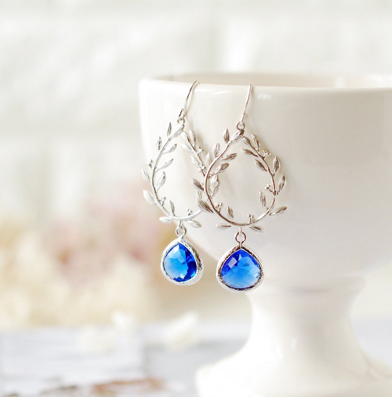 May include: Silver earrings with a delicate leaf design and dangling blue teardrop crystals.