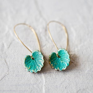 Op de afbeelding: Een paar gouden oorbellen met turquoise groene bladeren als hanger. De bladeren hebben een getextureerd oppervlak en een gouden rand.