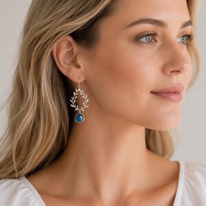 May include: Silver-toned earrings featuring a delicate wreath design with dangling blue gemstone pendants. The earrings are a stylish accessory, perfect for adding a touch of elegance to any outfit. The earrings are lightweight and comfortable for all-day wear.