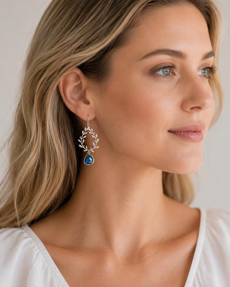 May include: Silver-toned earrings featuring a delicate wreath design with dangling blue gemstone pendants. The earrings are a stylish accessory, perfect for adding a touch of elegance to any outfit. The earrings are lightweight and comfortable for all-day wear.