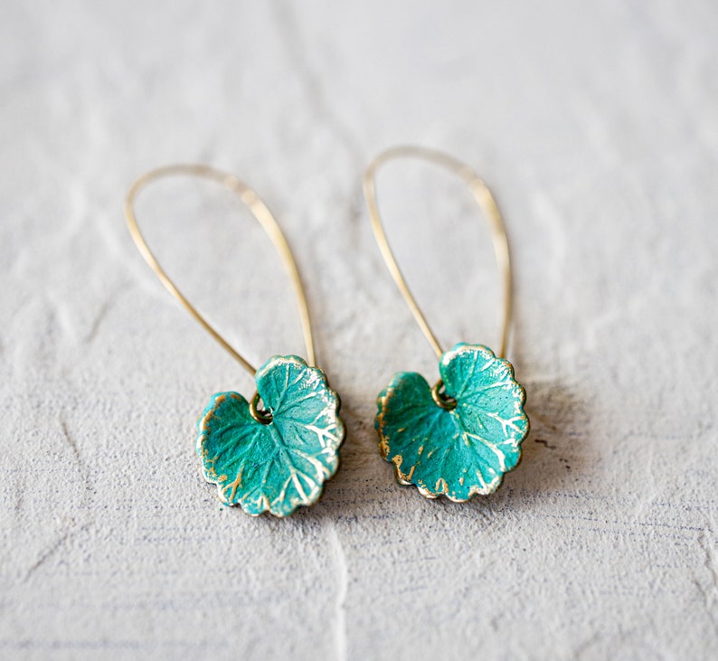 Op de afbeelding: Een paar gouden oorbellen met turquoise groene bladeren als hanger. De bladeren hebben een getextureerd oppervlak en een gouden rand.