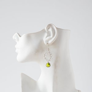 May include: Silver dangle earrings with a green gemstone and a leaf design.