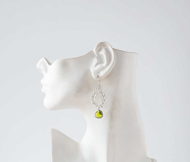 May include: Silver dangle earrings with a green gemstone and a leaf design.