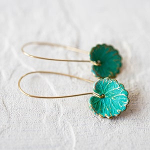 Op de afbeelding: Een paar gouden oorbellen met turquoise groene bladeren. De oorbellen zijn gemaakt van draad en hebben een eenvoudig ontwerp.