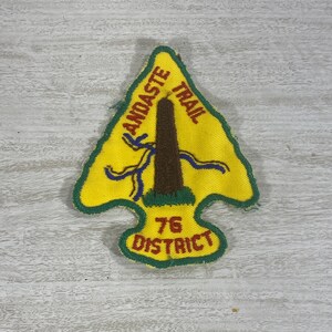May include: A yellow and green embroidered patch with a brown tree and blue ribbons. The text "Andaste Trail" is written in red on the patch. The text "76 District" is written in red on the bottom of the patch.