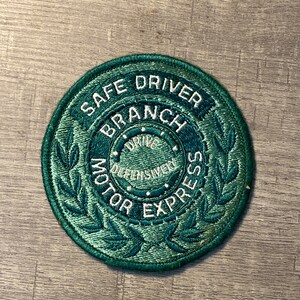 May include: Green embroidered patch with the text "Safe Driver Branch Motor Express" and a smaller circle with the text "Drive Defensively".