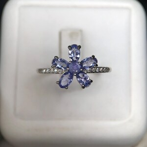 Peut inclure: Bague en argent orn&eacute;e d'une fleur compos&eacute;e de six pierres bleues claires. La monture de la bague est orn&eacute;e de petits brillants transparents. Les p&eacute;tales de la fleur sont bleu clair, sur fond blanc.