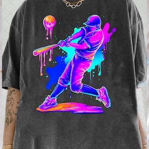 May include: Dark grey t-shirt with a neon graphic of a baseball player swinging a bat. The design features a baseball with dripping paint and colourful splatter effects, creating a dynamic sports theme.