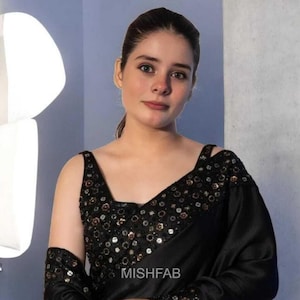 May include: Black saree with intricate sequin detailing on the neckline, sleeves, and shoulder straps. The saree features a V-neck design and is made of a flowing fabric. The text "MISHFAB" is visible on the garment.