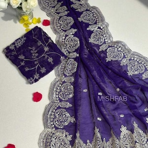Puede incluir: Un sari de color púrpura intenso con intrincados bordados plateados a lo largo de los bordes y contornos. La tela está drapeada, mostrando los detallados adornos y una pieza de blusa bordada a juego. Incluye el texto "MISHFAB".