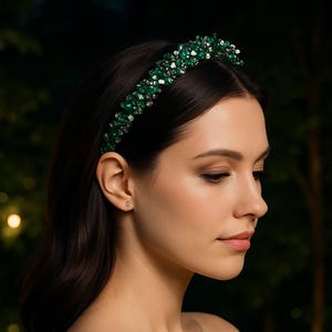 May include: A green beaded headband with a dark background. The headband is adorned with emerald green and silver-toned beads. The woman in the image is wearing the headband and has dark hair and a fair complexion.