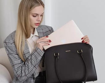 May include: A black leather laptop bag with a curved top and two handles. The bag has gold-colored hardware and is being opened to reveal a laptop. The person is wearing a plaid blazer and black pants.