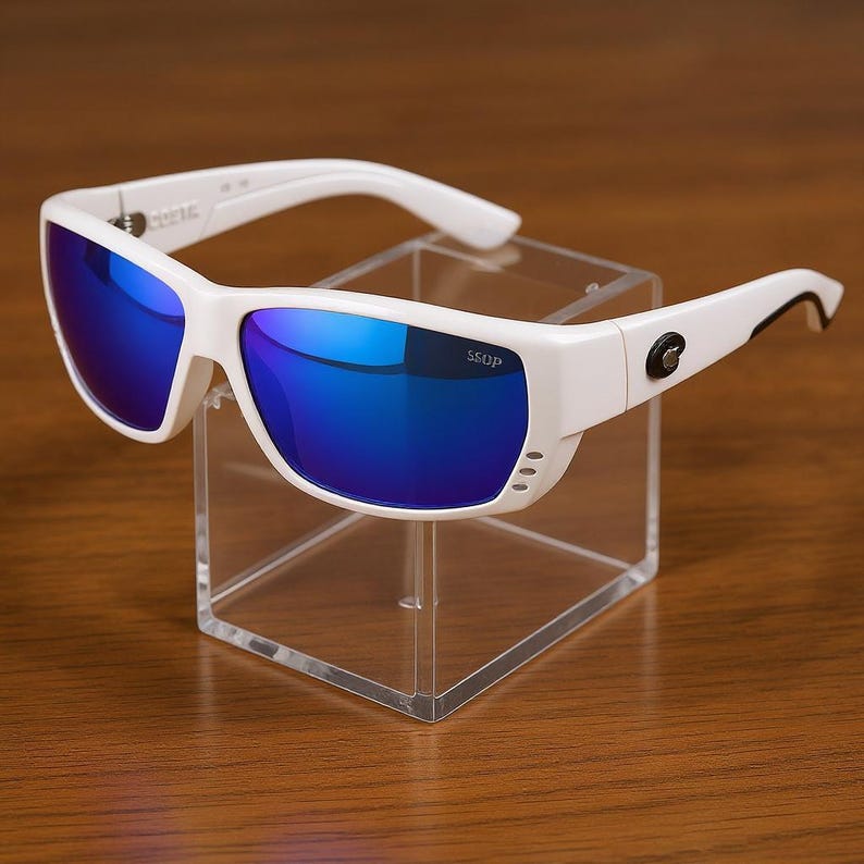 Puede incluir: Gafas de sol blancas con lentes azules espejadas. Las gafas tienen una montura rectangular con un dise&ntilde;o curvo y el texto "SSOP" es visible en la lente. Las gafas se exhiben en un soporte de acr&iacute;lico transparente.