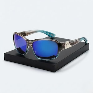 May include: Sunglasses with a blue mirrored lens and a gray and blue frame. The temples have a blue accent and a silver emblem. The sunglasses are displayed on a black surface.