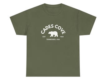 Puede incluir: Camiseta verde oliva con un diseño blanco. El diseño incluye las palabras "Cades Cove", una silueta de oso y el texto "EST 1934 Tennessee, USA". La camiseta está hecha de un material suave y cómodo.
