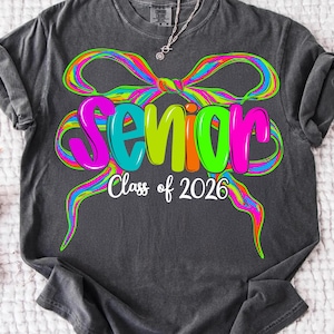 May include: Dark grey t-shirt featuring a vibrant bow design and the word "Senior" in multi-coloured letters. The text "Class of 2026" is below. A casual, comfortable style of shirt.