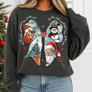 May include: Dark gray sweatshirt featuring a Christmas bow design with a reindeer, snowman, and Santa Claus. The bow includes a Christmas tree and the text "It's the most wonderful time of the year". Festive holiday apparel.