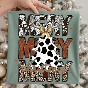 May include: A sage green Christmas-themed design with the words "MERRY CHRISTMAS MERRY" in various fonts and patterns. The design includes a cow print Christmas tree, antlers, and a gold bow.