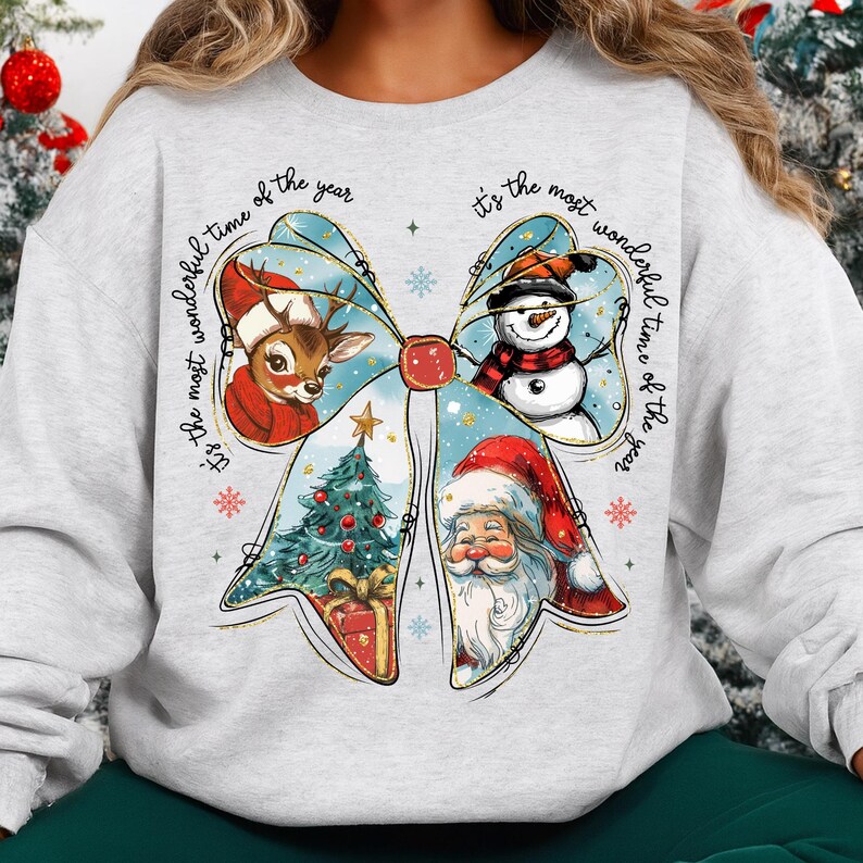 May include: A light gray sweatshirt featuring a festive bow design with a reindeer, snowman, Christmas tree, and Santa Claus. The text "It's the most wonderful time of the year" is printed around the bow.