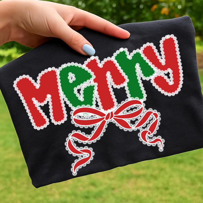 May include: Black t-shirt with the word "MERRY" in red and green, outlined with white lace. A red bow with white lace accents is below the word. The shirt is held by a hand with a light blue nail polish.