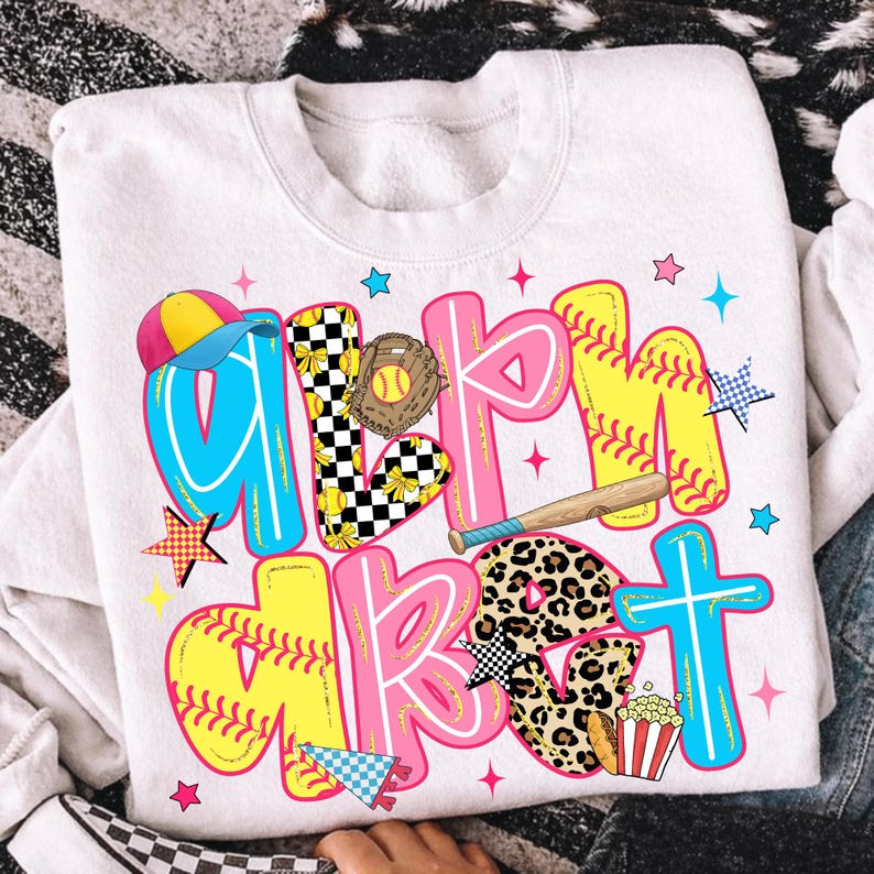 May include: White sweatshirt with a colorful softball-themed graphic. The design features the words "Girl's Market" in large, playful letters with baseball and softball elements, including a glove, bat, and popcorn.