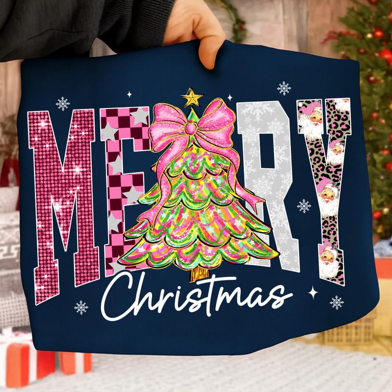 May include: Navy blue Christmas-themed graphic tee with the words "MERRY Christmas" in a festive design. The "M" is pink with sequins, the "E" is checkered, and the "R" and "Y" are white. A colorful Christmas tree with a pink bow is in the center.