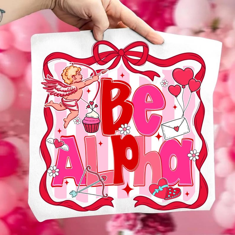May include: A white tote bag with a Valentine's Day design. The design features the words "Be Alpha" in red and pink, along with illustrations of Cupid, hearts, flowers, and a bow and arrow. A red ribbon frames the design.