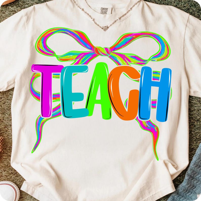May include: Cream-colored t-shirt with the word "TEACH" in vibrant, multi-colored letters. A neon-colored bow design arches above the word, adding a playful touch. The shirt is made of a soft material and is suitable for teachers.