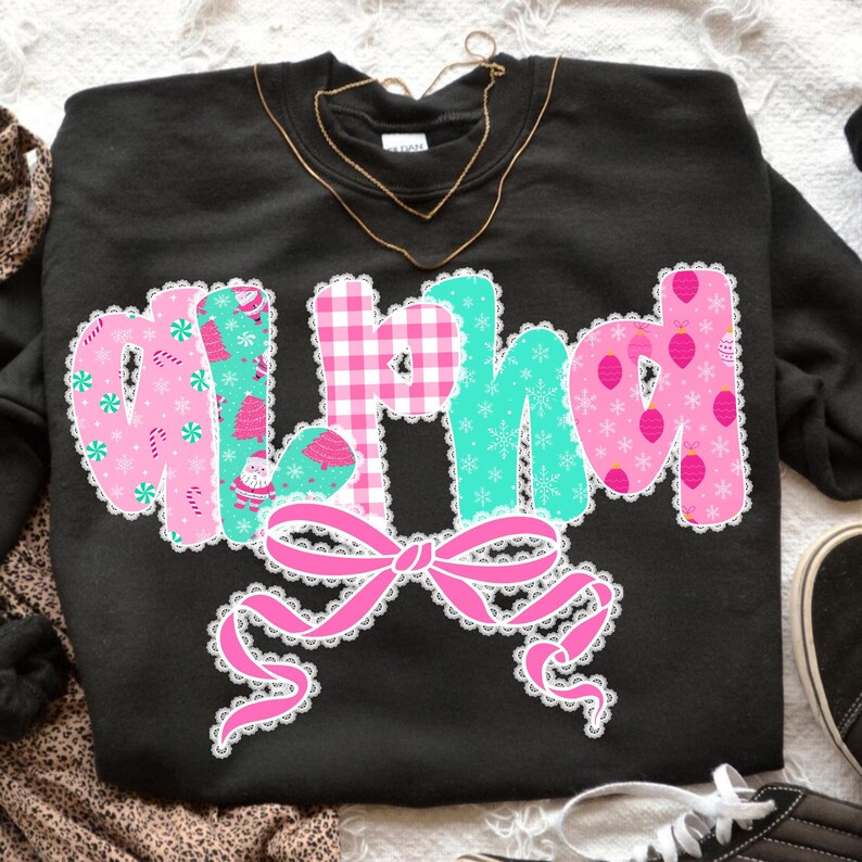 Pu&ograve; includere: Felpa nera con la scritta "Mirth" in un design festivo. Le lettere sono rosa, turchese e a quadretti, con motivi natalizi e un fiocco rosa. Una collana d'oro &egrave; drappeggiata sulla felpa.