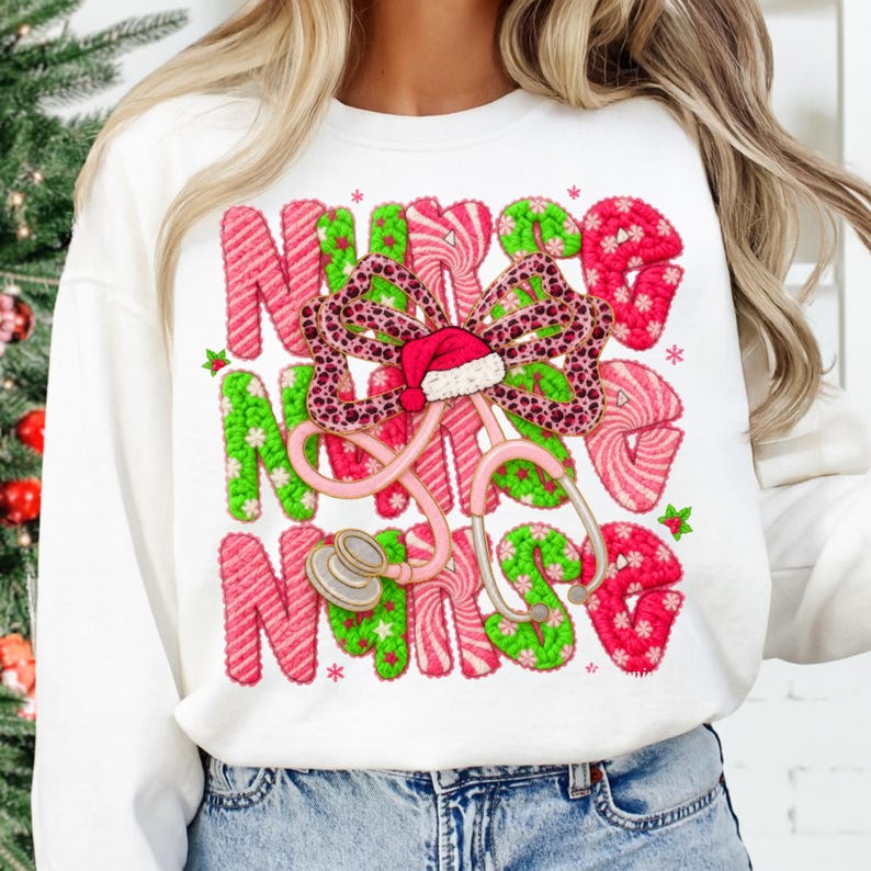 May include: White sweatshirt with the word "NURSE" in pink and green candy cane-style letters. A pink stethoscope and a bow with a Santa hat are in the center. The bow has a leopard print design.