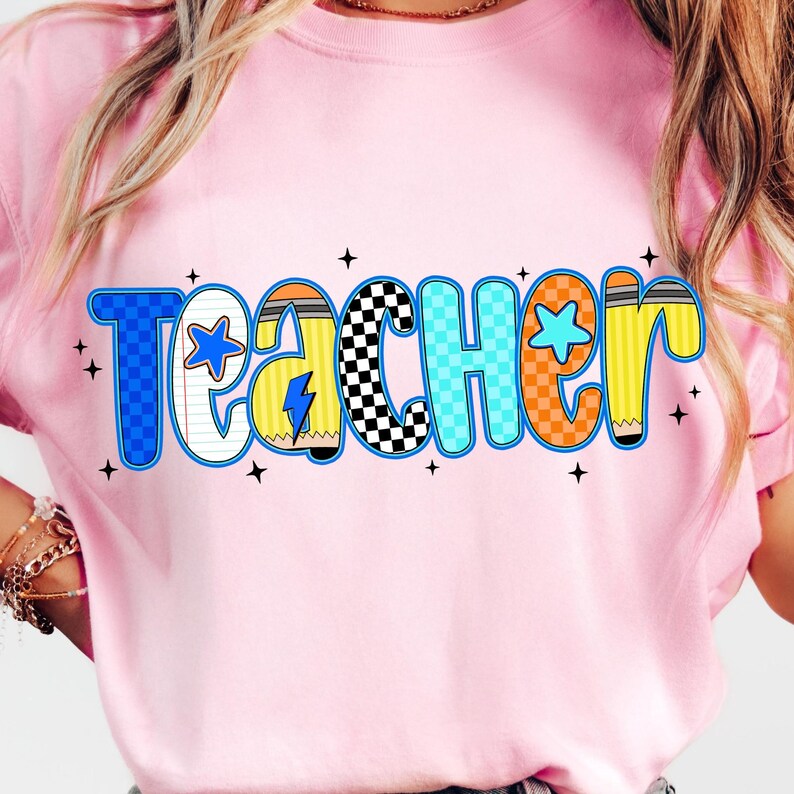 May include: Pink t-shirt with the word "Teacher" in a colorful, playful font. The letters are outlined in blue, orange, and yellow, with star and pencil details. The shirt is a light pink color.