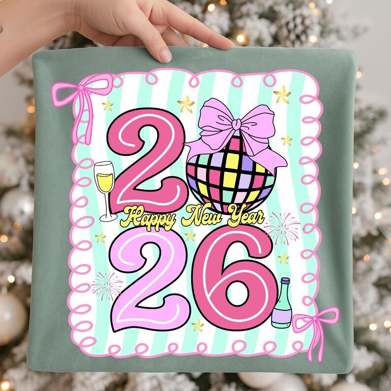 May include: A decorative pillow with a festive design for the New Year. The design features the numbers "26" in pink, a disco ball, champagne, and the words "Happy New Year". The pillow has a light green border and pink bows.