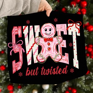 May include: Black square with the words "SWEET" and "TWISTED" in pink and white, along with a gingerbread man. The gingerbread man has a red bow tie and buttons. Pink bows and snowflakes are also featured in the design.