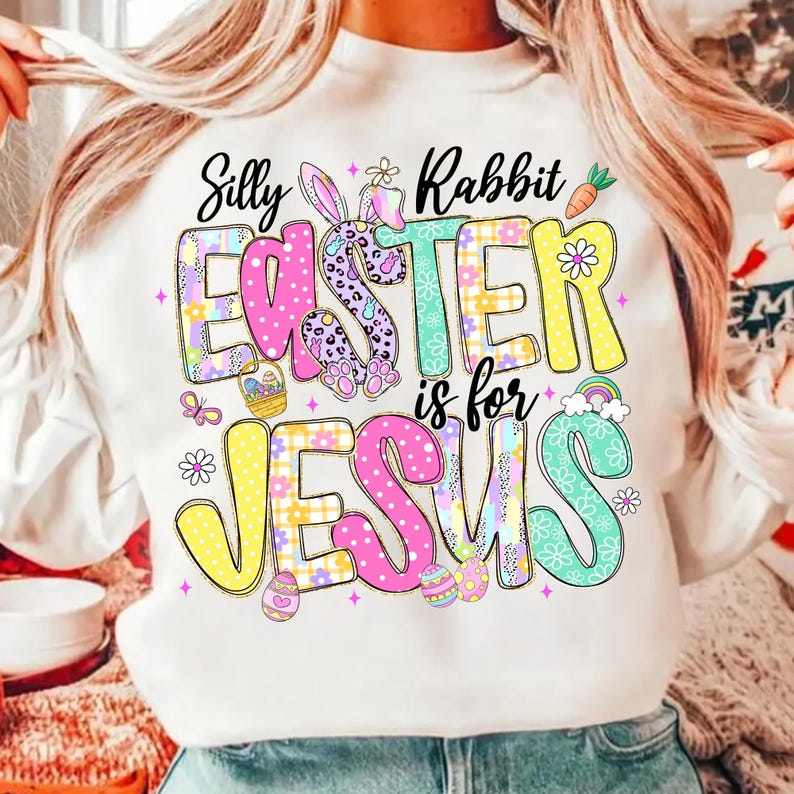 May include: White sweatshirt with a colorful Easter graphic. The design features the text "Silly Rabbit Easter is for Jesus" in a playful font, along with Easter eggs, a bunny, and a rainbow.