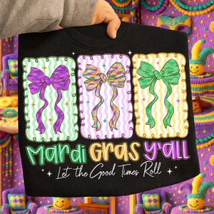 May include: Black sweatshirt with three colorful bow designs in purple, yellow, and green. The text "Mardi Gras y'all" and "Let the Good Times Roll" are printed below the bows. The design is festive and celebratory.