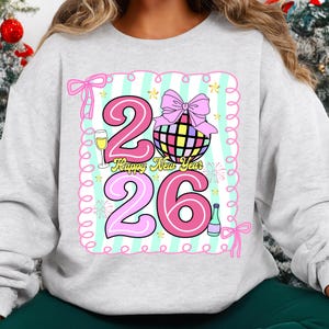 May include: A light gray sweatshirt featuring a colorful graphic design for the New Year. The design includes the numbers "26", a disco ball, champagne, and the text "Happy New Year". The design is outlined with pink and light blue accents.