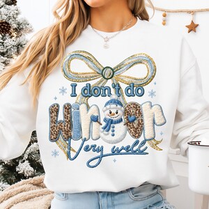 May include: White sweatshirt with a large embroidered design. The design features a bow, snowflakes, and a snowman with the text "I don't do winter very well". The word "winter" has a leopard print pattern.