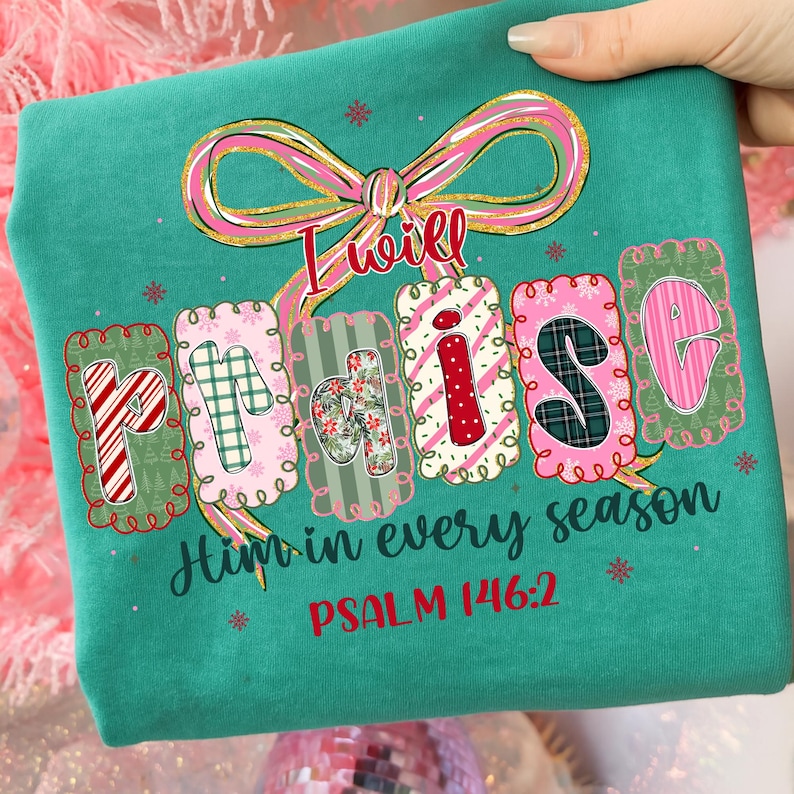 May include: Teal-colored t-shirt with the words "I will PRAISE Him in every season" in a decorative font. The word "PRAISE" is in individual letter blocks with various patterns. The text "PSALM 146:2" is printed in red.